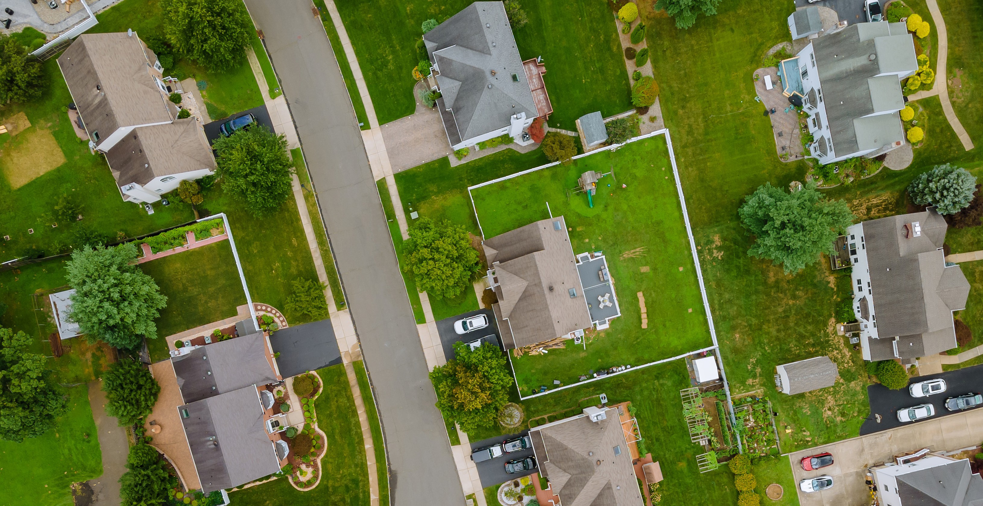 Aerial view of suburban front yards dominated by monoculture lawns — the paradigm Holon Gardens is transforming