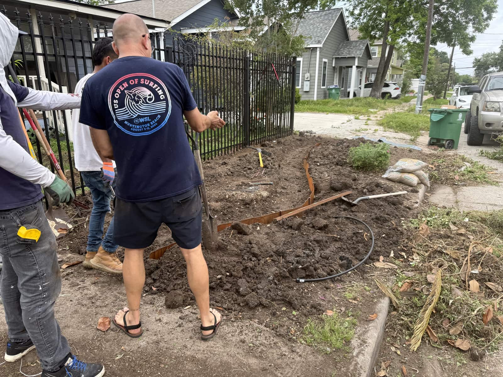 Two people digging and clearing a curbside bed by an iron fence