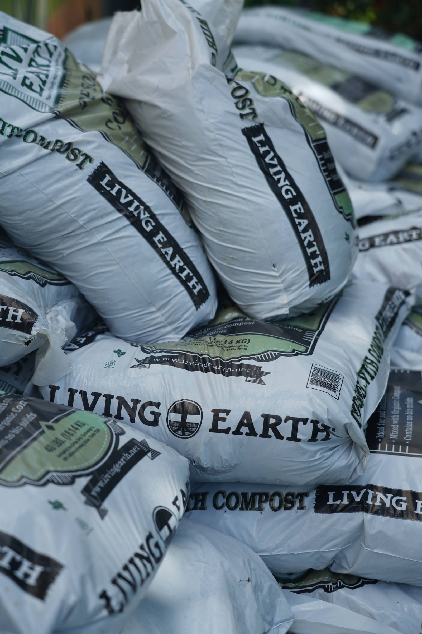 Bags of Living Earth compost stacked at the edge of a garden